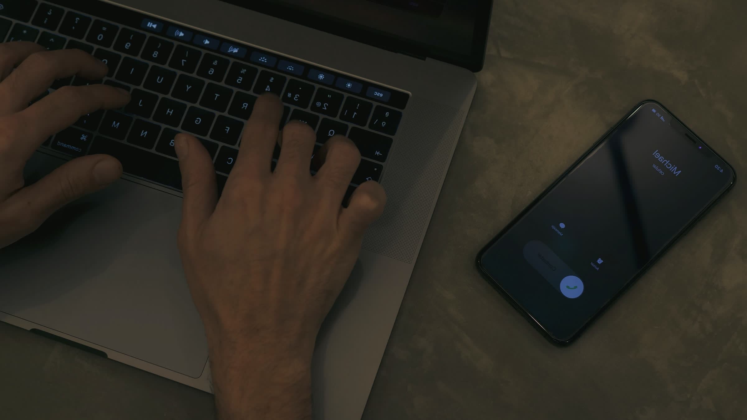 Hands on a laptop next to a phone showing an incoming call