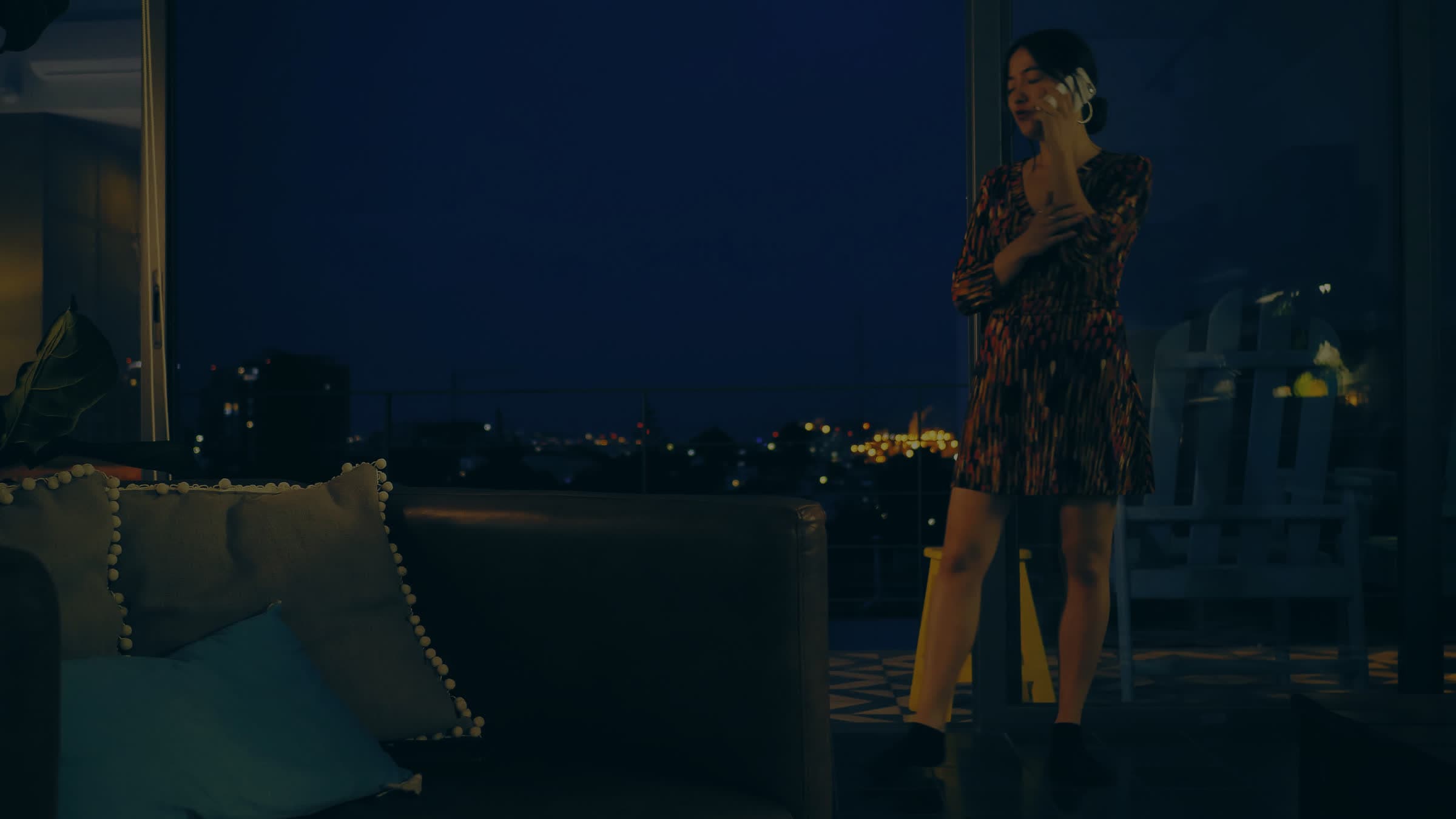 A woman on the phone by a window at night, the city lights behind her